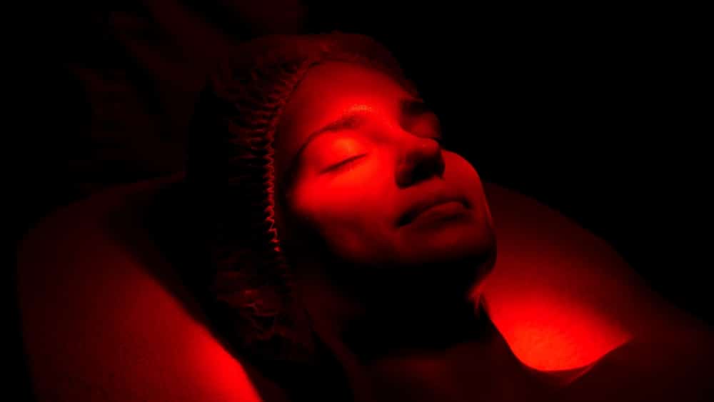 Cosmetologist performing red light therapy using LED technology for facial rejuvenation.