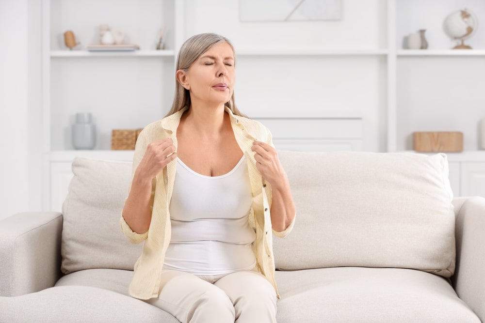 Woman fans herself in frustration during a hot flash while considering HRT