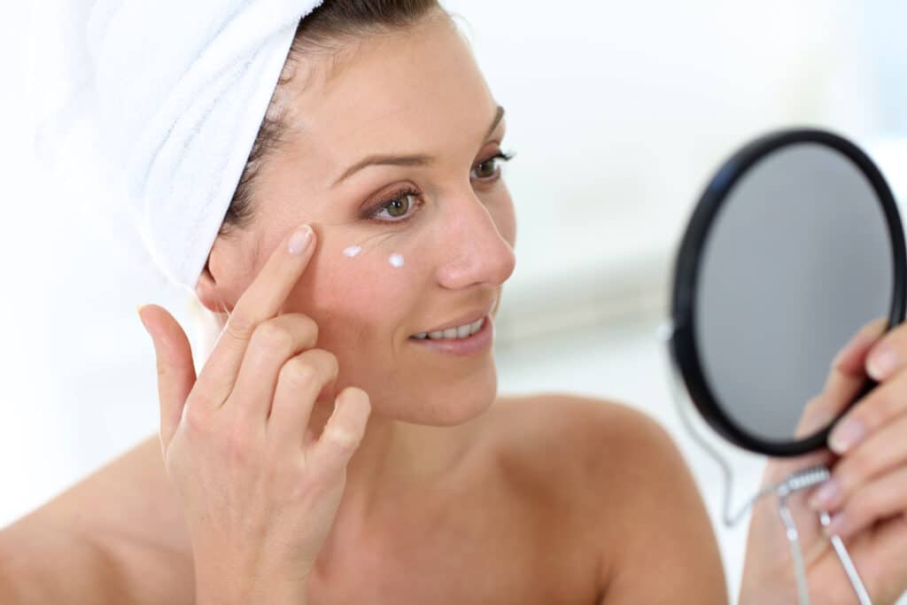 Woman applies face cream while looking in a handheld mirror as she considers a VISIA skin analysis