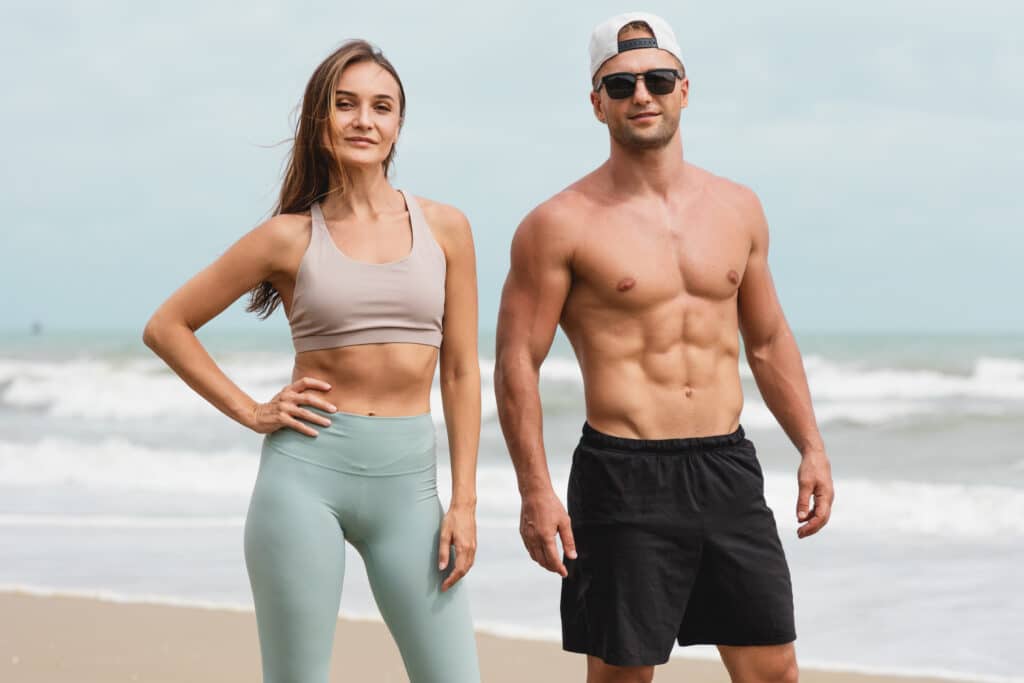 Fit and healthy couple on the beach, showing off their toned bodies after Emsculpt NEO treatments